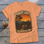 Peach t-shirt with "The Porch Light is Always On" cabin sunset graphic.