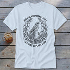 White crewneck t-shirt featuring a black graphic of a bird perched on a wooden post, surrounded by corn stalks and the text "When the whippoorwill calls, it's time to plant corn."