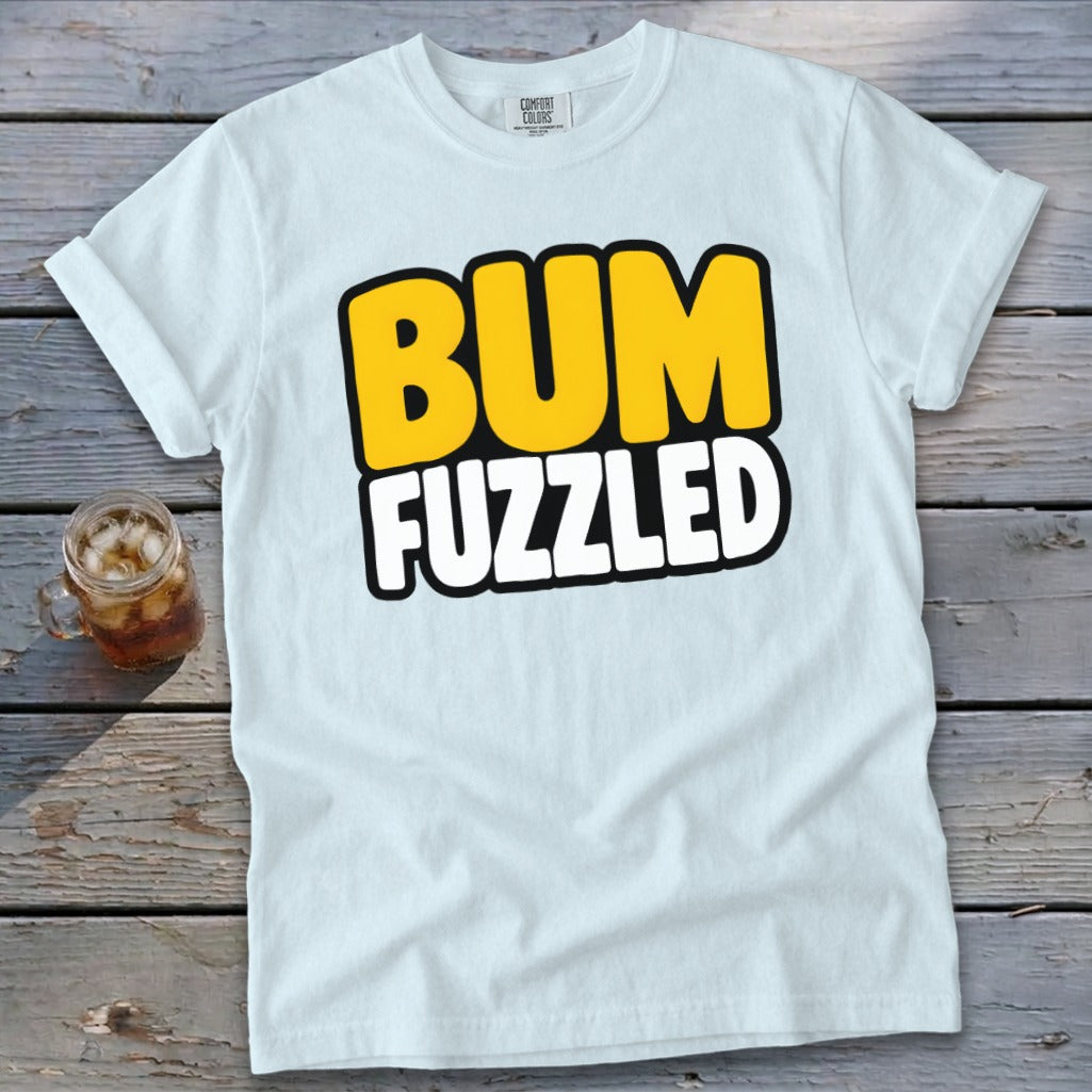 A light blue t-shirt printed with the text Bum Fuzzled, lying on a wooden surface with a glass of iced tea.