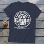 A navy blue t-shirt with white text reading Certified Cornbread Judge and a graphic of a cornbread wheel.