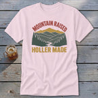 Light pink t-shirt featuring a retro mountain and forest graphic with the text Mountain Raised Holler Made.