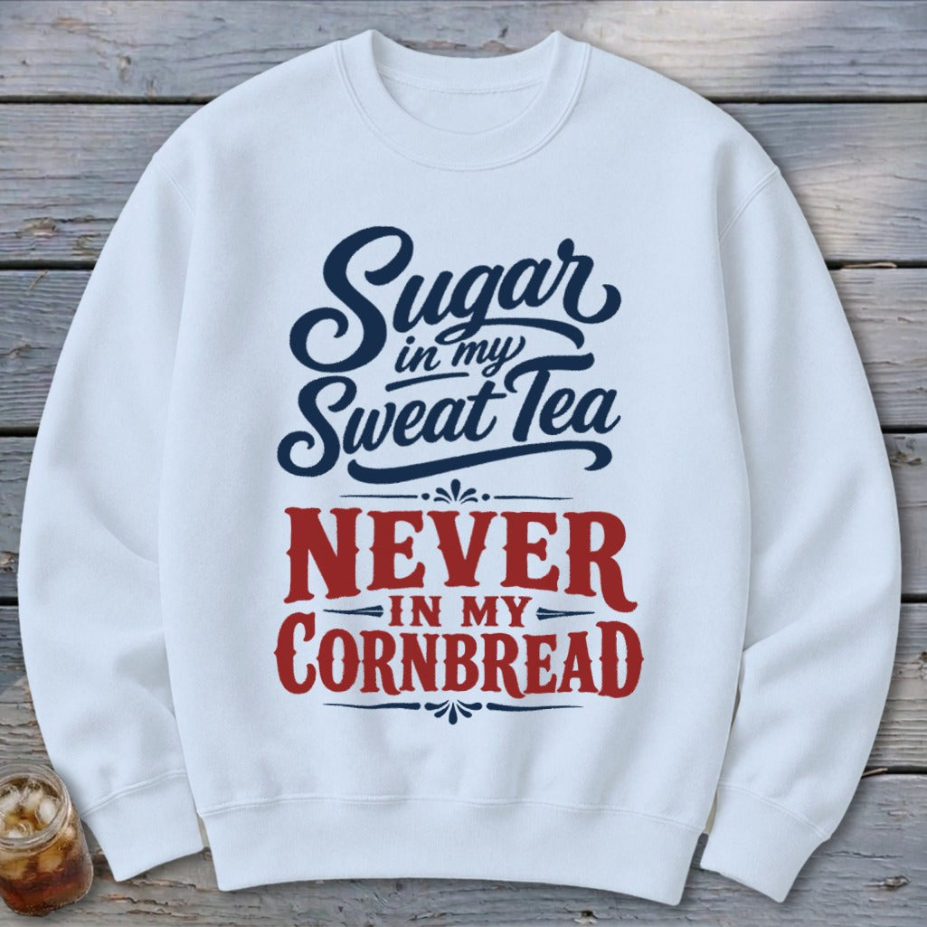 A white crewneck sweatshirt features blue text reading "Sugar in my Sweat Tea" above red text reading "NEVER IN MY CORNBREAD".