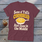Maroon t-shirt featuring text and a skillet graphic with cornbread, laid flat on a wooden surface.