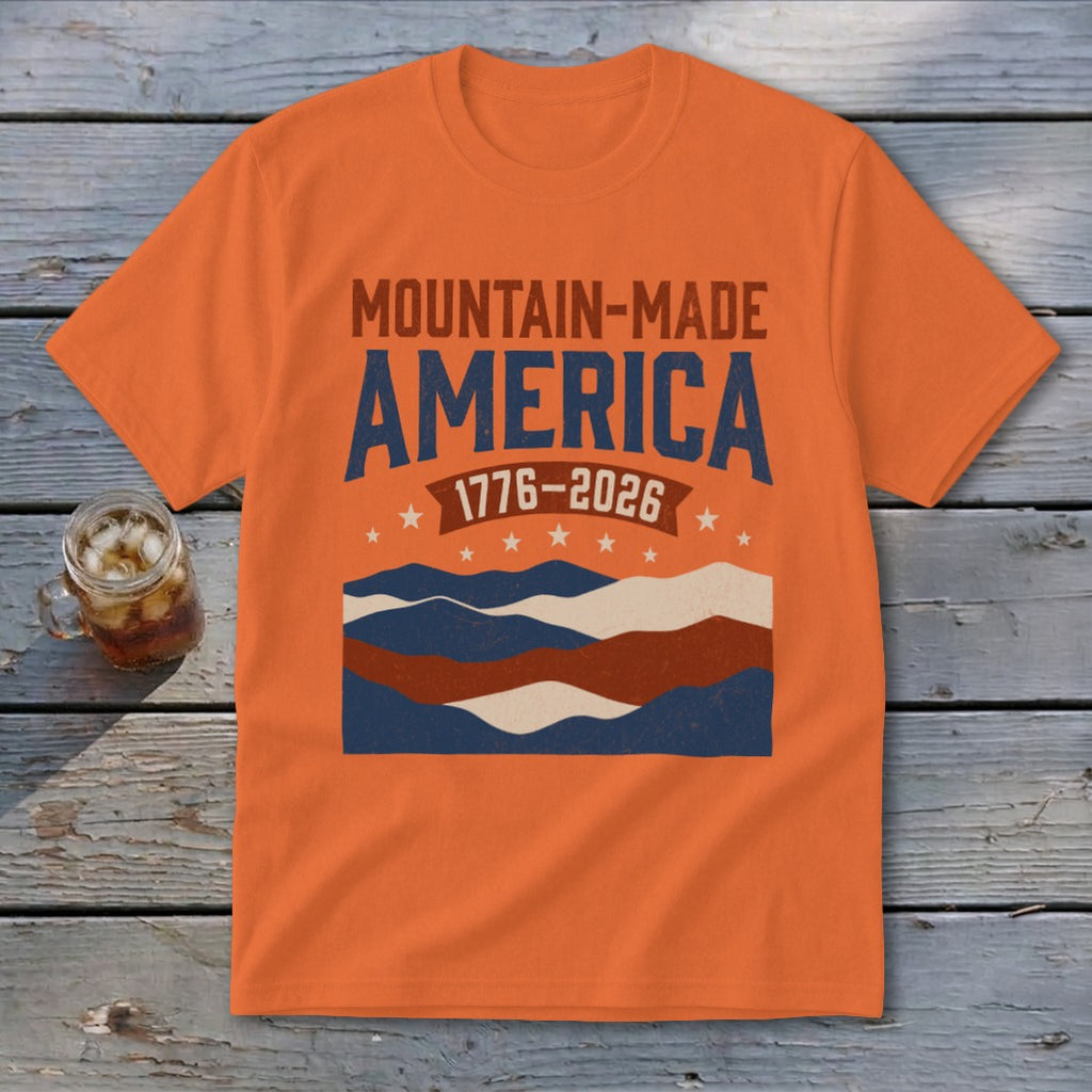 An orange short-sleeved t-shirt featuring a distressed mountain graphic with text that reads Mountain-Made America and 1776-2026.