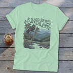 Mint t-shirt with a bird on a branch above a river and mountains, text reads "No place sounds like home".
