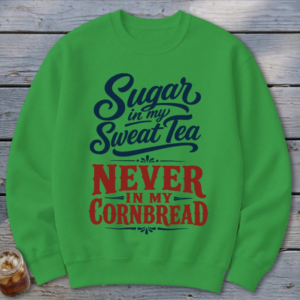 Green crewneck sweatshirt featuring the blue and red text "Sugar in my Sweat Tea NEVER IN MY CORNBREAD."