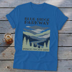 Blue t-shirt featuring a stylized landscape graphic of mountains, trees, and a winding road.