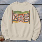 Cream crewneck sweatshirt featuring a graphic of three vintage quilts hanging on a clothesline outdoors.