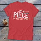 Red t-shirt with white text reading "JUST A PIECE DOWN THE ROAD".