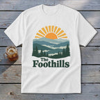 White t-shirt with mountain landscape graphic and text "The Foothills".