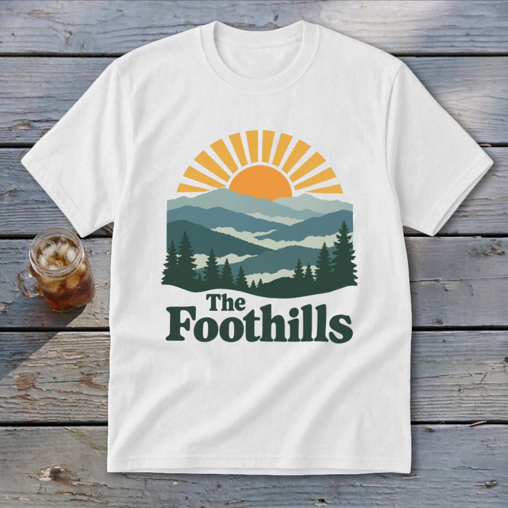White t-shirt with mountain landscape graphic and text "The Foothills".