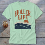 Light green t-shirt with the orange text HOLLER LIFE above a sunset landscape graphic.