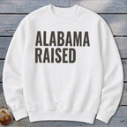 White crewneck sweatshirt with "ALABAMA RAISED" text in dark grey.