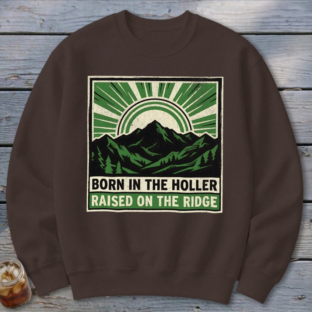 Brown crewneck sweatshirt featuring a graphic of mountains and sunburst with the text BORN IN THE HOLLER RAISED ON THE RIDGE.