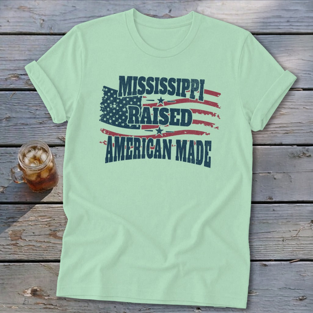 Light green t-shirt featuring the text Mississippi Raised American Made and a distressed American flag graphic.