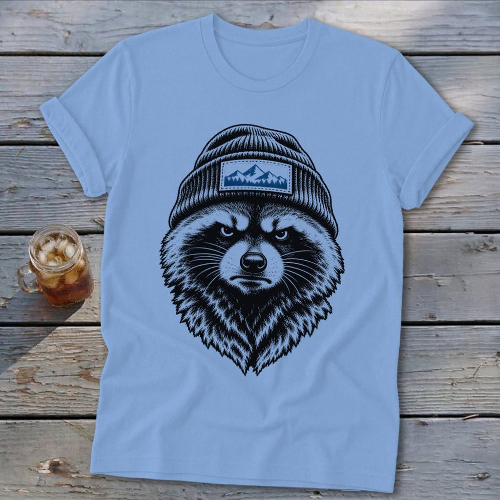 Light blue t-shirt featuring a black and white illustration of a grumpy raccoon wearing a beanie with a mountain patch.