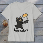 A light grey V-neck t-shirt featuring a cartoon black bear flipping a pancake from a skillet, with the text hoecakes below.