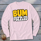 A light pink long-sleeve t-shirt with the words BUM FUZZLED printed in yellow and white block letters on the chest, lying flat on a wooden surface.