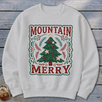 Off-white crewneck sweatshirt featuring a graphic of a Christmas tree with the text MOUNTAIN MERRY.