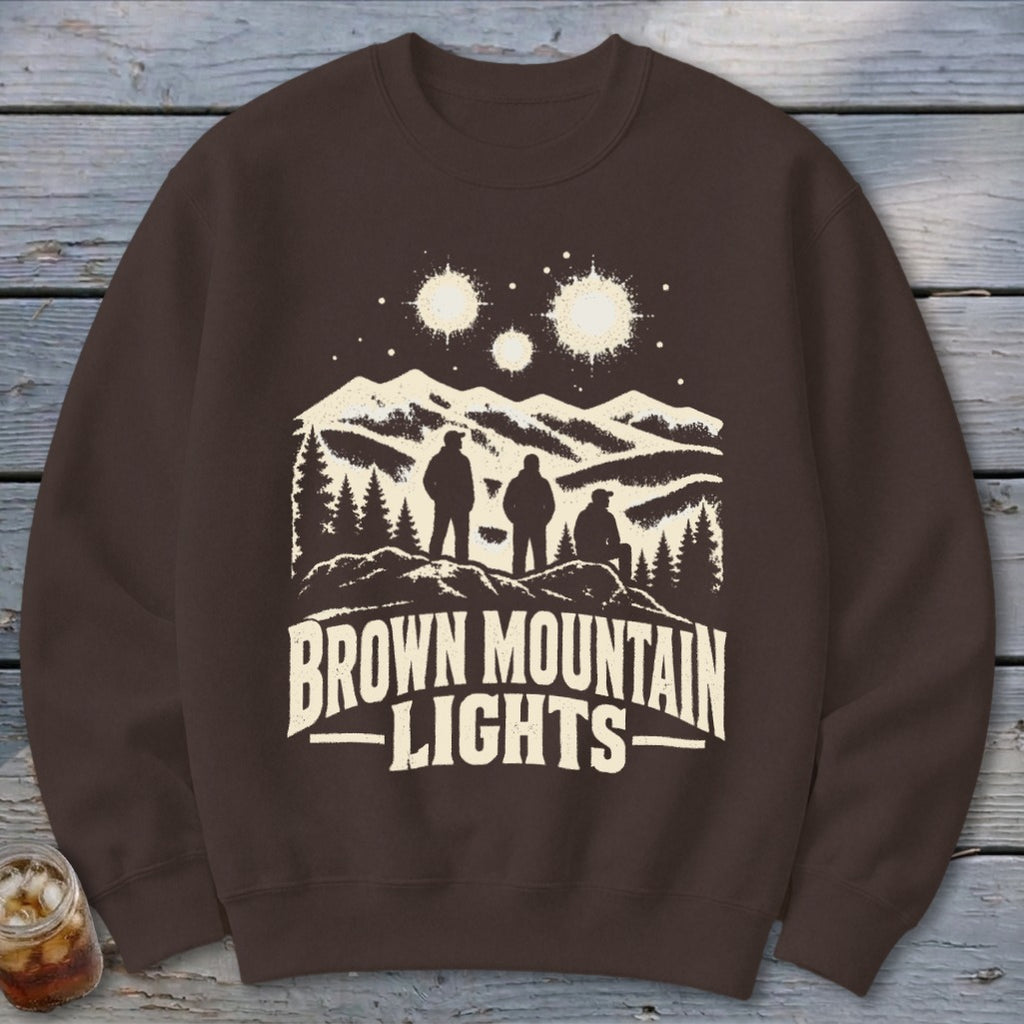 Brown crewneck sweatshirt featuring a graphic of three figures, mountains, glowing lights, and the text Brown Mountain Lights.