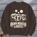 Brown crewneck sweatshirt featuring a graphic of three figures, mountains, glowing lights, and the text Brown Mountain Lights.