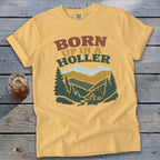 Yellow t-shirt with "BORN UP IN A HOLLER" text and mountain cabin graphic.