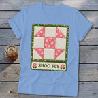 Light blue t-shirt featuring a "Shoo Fly" quilt block design with pink floral accents.