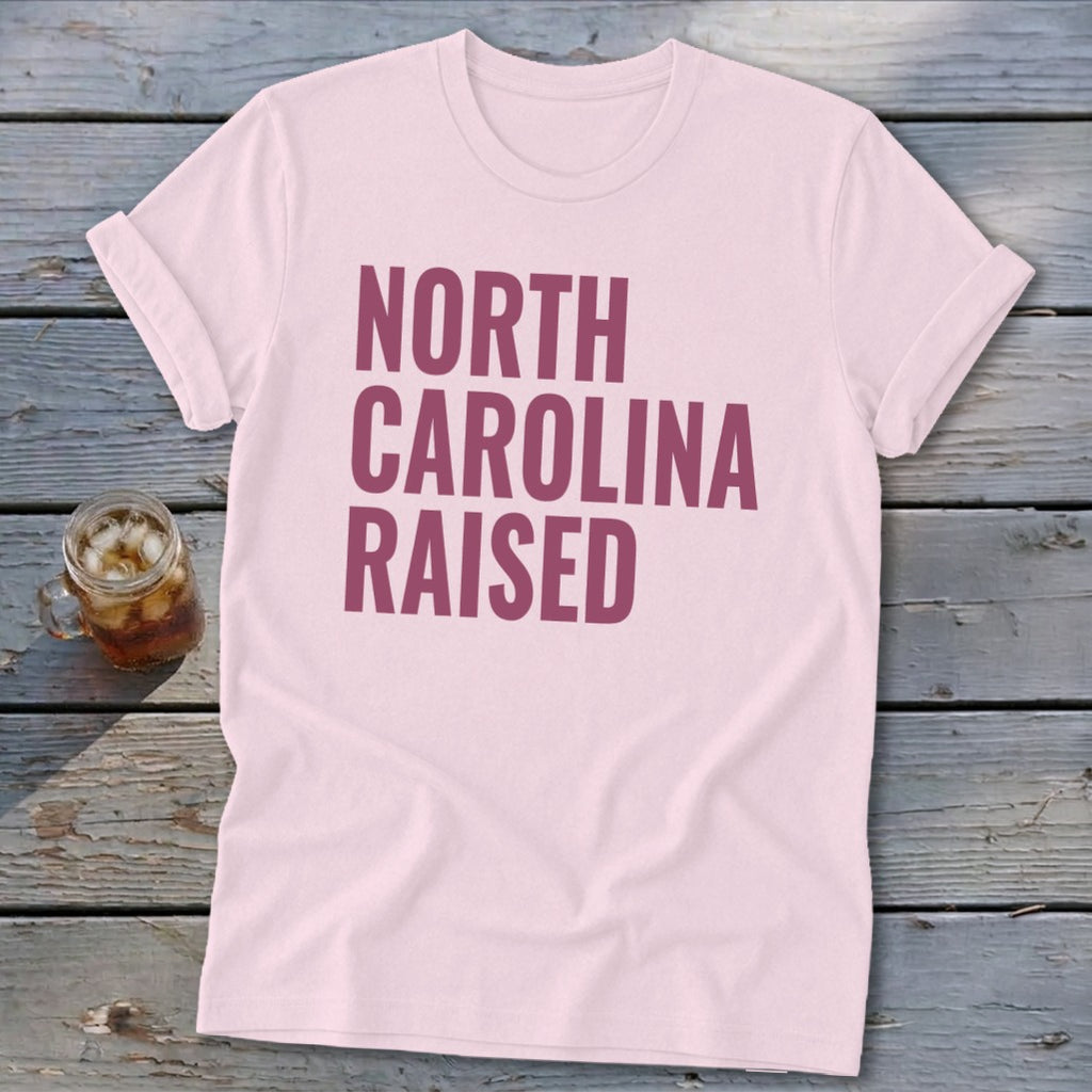 Pink t-shirt with "NORTH CAROLINA RAISED" in maroon text.