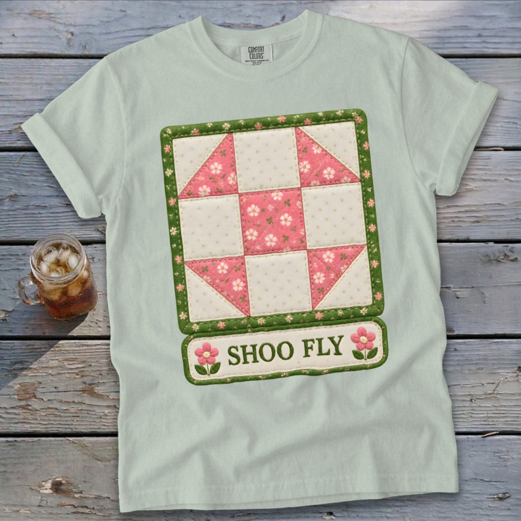 Light green t-shirt with a pink and white quilt square graphic that says "SHOO FLY".