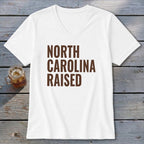 White v-neck t-shirt with brown text reading "North Carolina Raised."