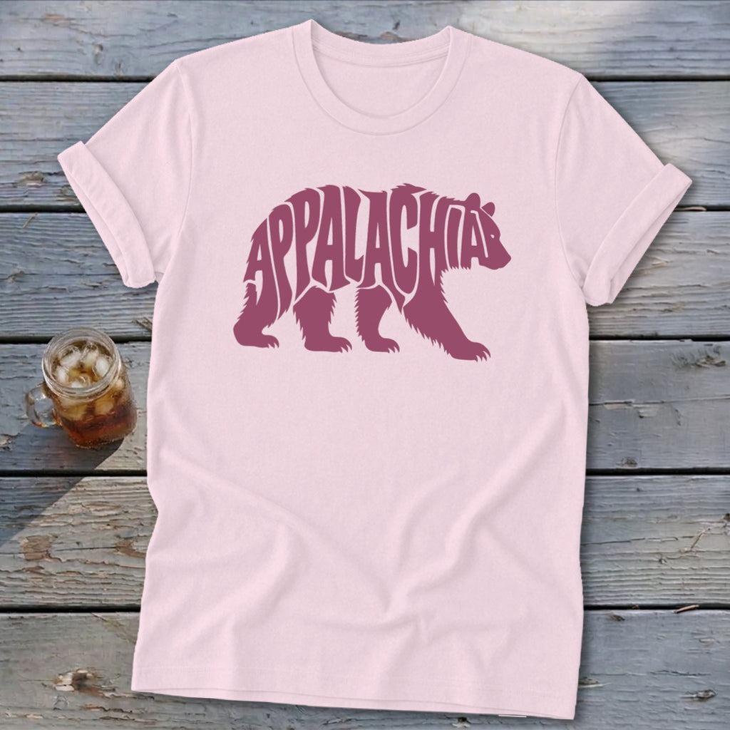 Light pink t-shirt featuring a maroon bear graphic containing the text Appalachia, laid on weathered wood.