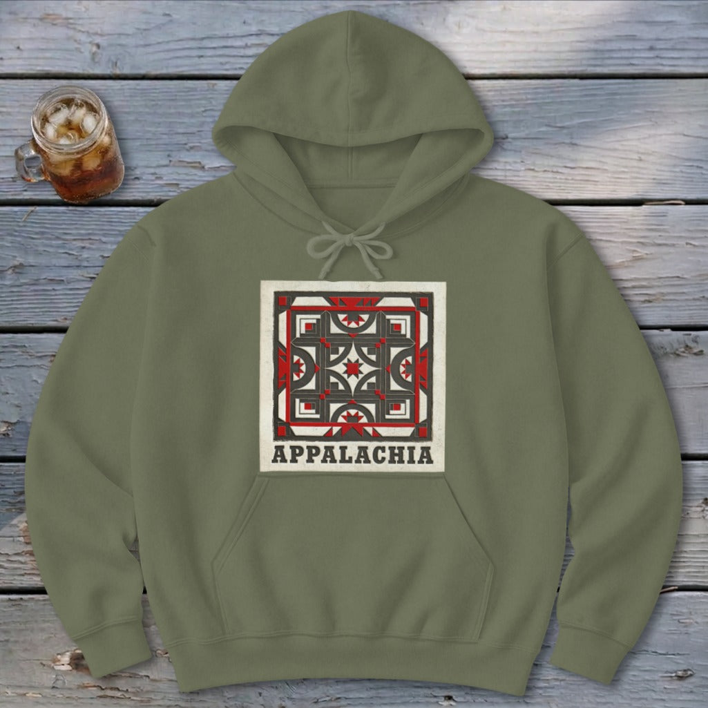 An olive green hoodie featuring a square geometric graphic with the text Appalachia underneath, lying on a wooden surface.