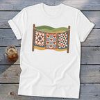 A white t-shirt featuring a graphic of three patchwork quilts hanging on a clothesline against a landscape.