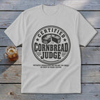 Light gray t-shirt with a vintage-style circular graphic reading Certified Cornbread Judge and humorous disqualification criteria below.