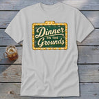 A light gray t-shirt with a vintage green and yellow sign graphic that reads Dinner on the Grounds.