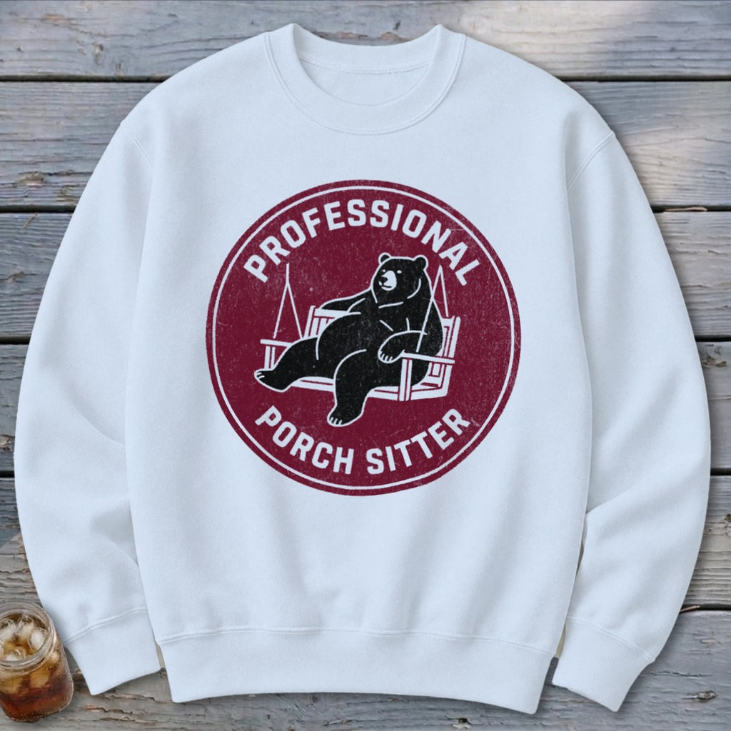 White crewneck sweatshirt with a maroon circular graphic of a bear lounging on a porch swing, reading Professional Porch Sitter.