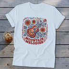 A white t-shirt featuring a folk-art guitar and sunflower graphic with the text "MOUNTAIN MELODIES".