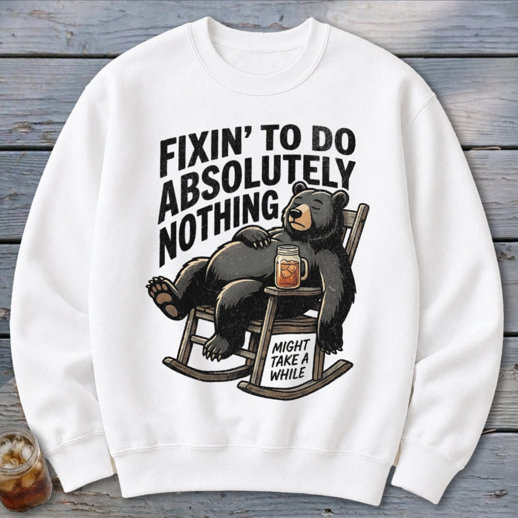 A white crewneck sweatshirt features an illustrated black bear relaxing in a rocking chair with a drink.