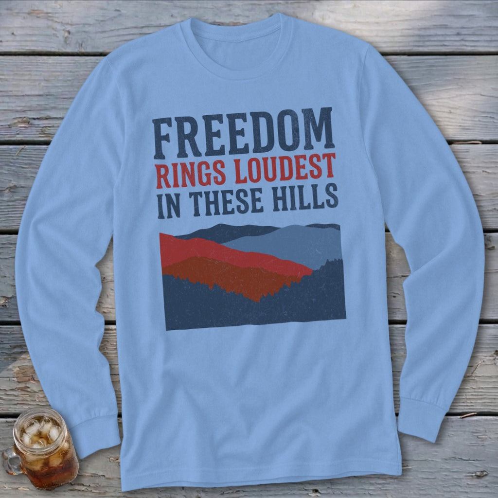 Light blue long-sleeve t-shirt with a graphic of layered hills and the text Freedom Rings Loudest in These Hills.