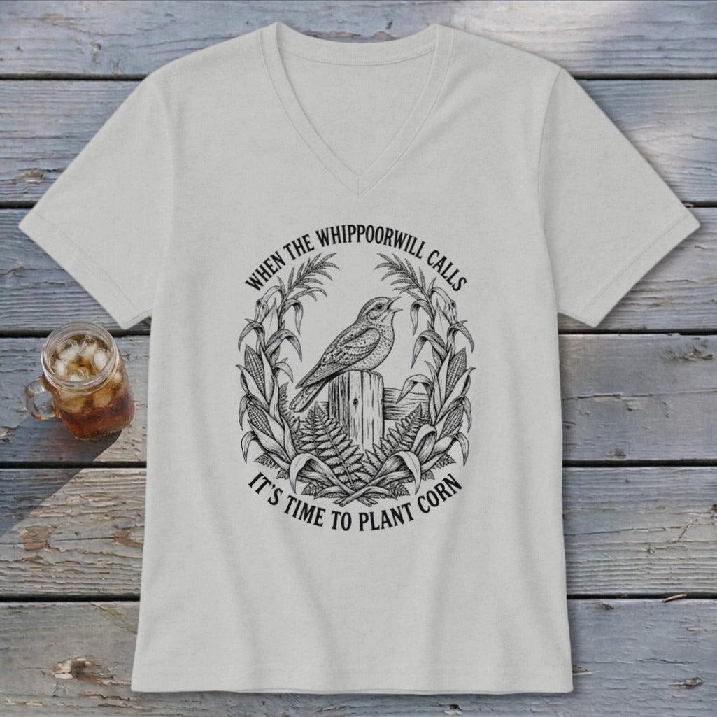 Light grey V-neck t-shirt featuring a black graphic of a bird on a post, framed by corn stalks, with the text WHEN THE WHIPPOORWILL CALLS IT'S TIME TO PLANT CORN.