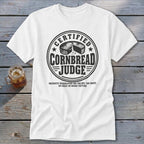 White t-shirt featuring a black graphic that reads Certified Cornbread Judge surrounding a cornbread wheel.