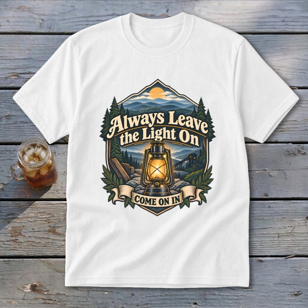 White t-shirt with graphic of lantern, mountains, trees, and text "Always Leave the Light On Come On In".