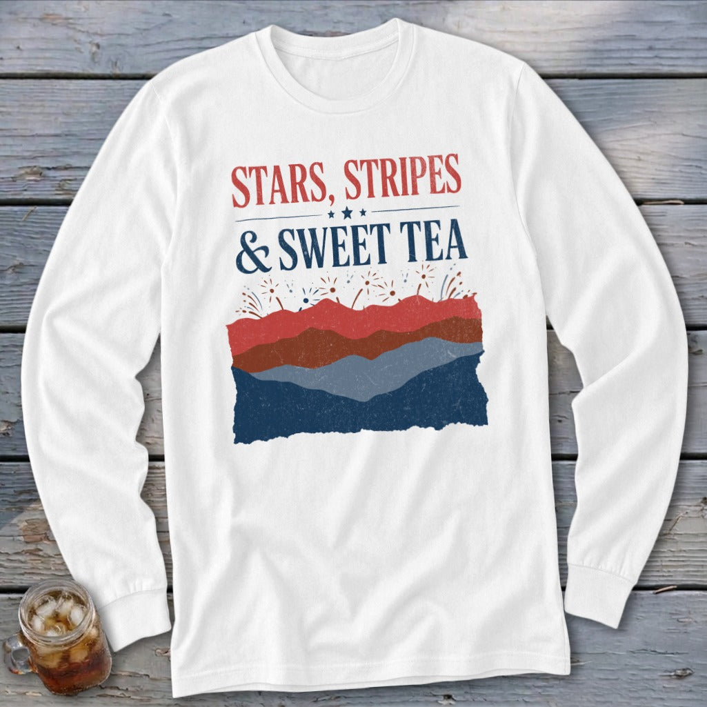 White long-sleeve t-shirt with red and blue text reading STARS STRIPES & SWEET TEA above layered hills and fireworks.