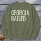 Olive green crewneck sweatshirt with "GEORGIA RAISED" text in light beige.