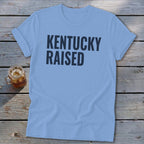 Light blue t-shirt with dark blue text "KENTUCKY RAISED" and a glass of iced tea.