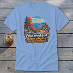 T-shirt with mountain landscape, autumn leaves, and text "Peak weekend. Same playlist. New overlook."
