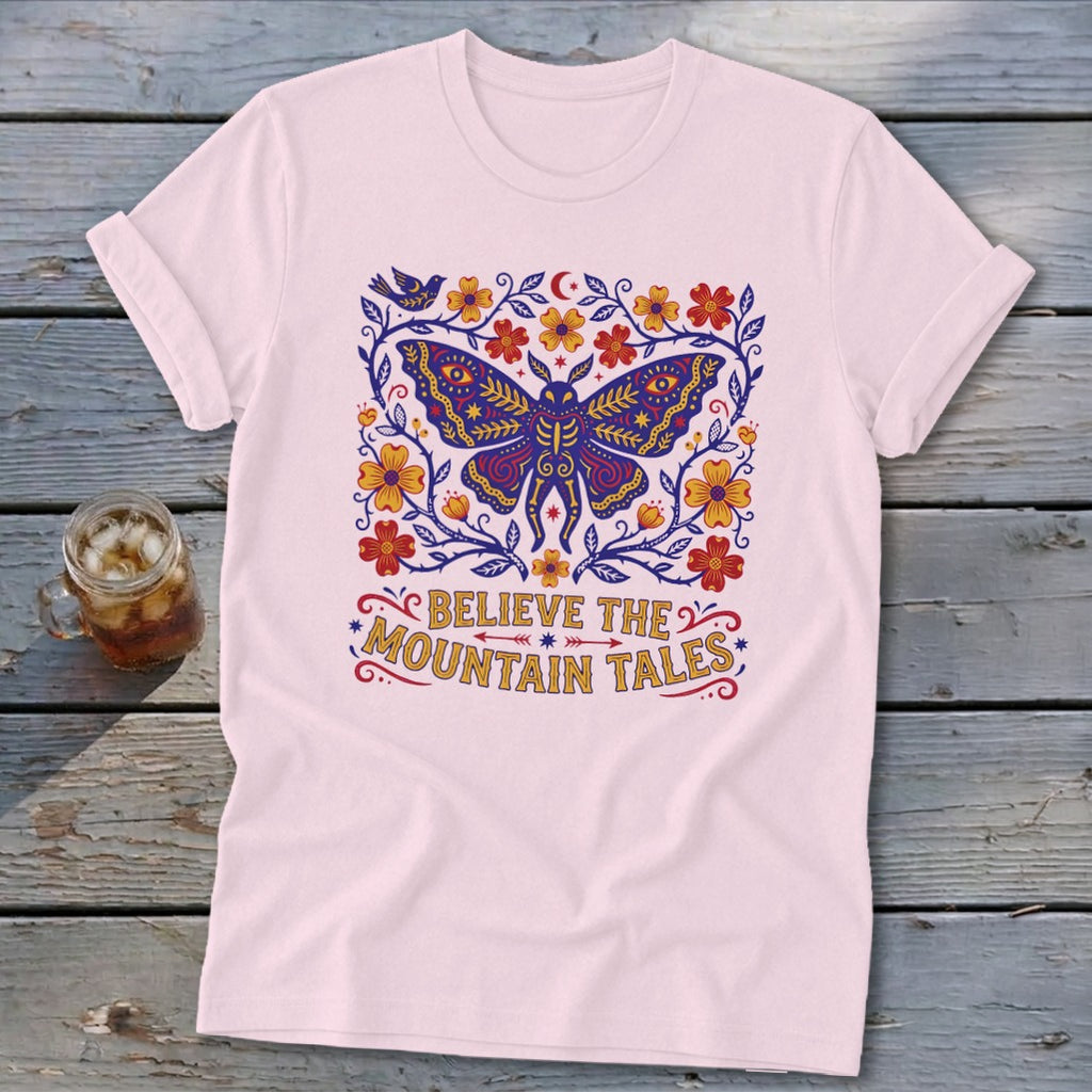 Light pink t-shirt with a colorful moth and floral design, saying "Believe The Mountain Tales".