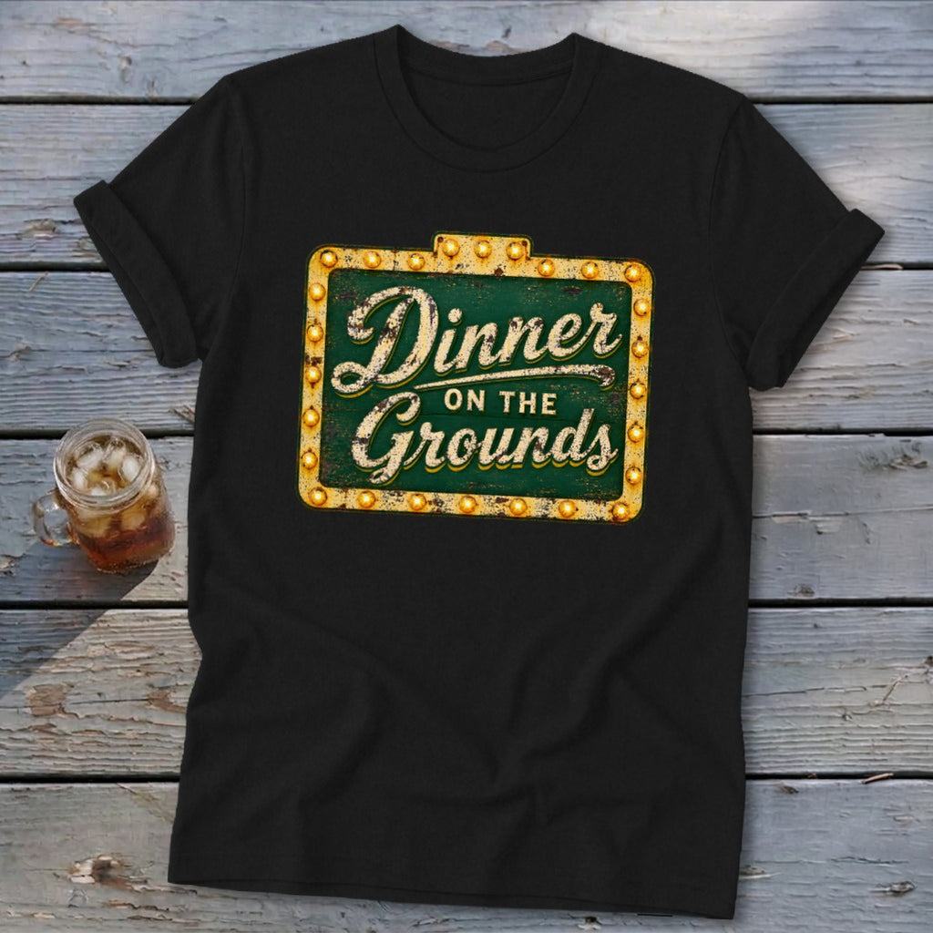 Black t-shirt featuring a green and gold marquee sign graphic that reads Dinner on the Grounds.