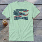 Light green t-shirt with distressed American flag graphic and text that reads North Carolina Raised American Made.