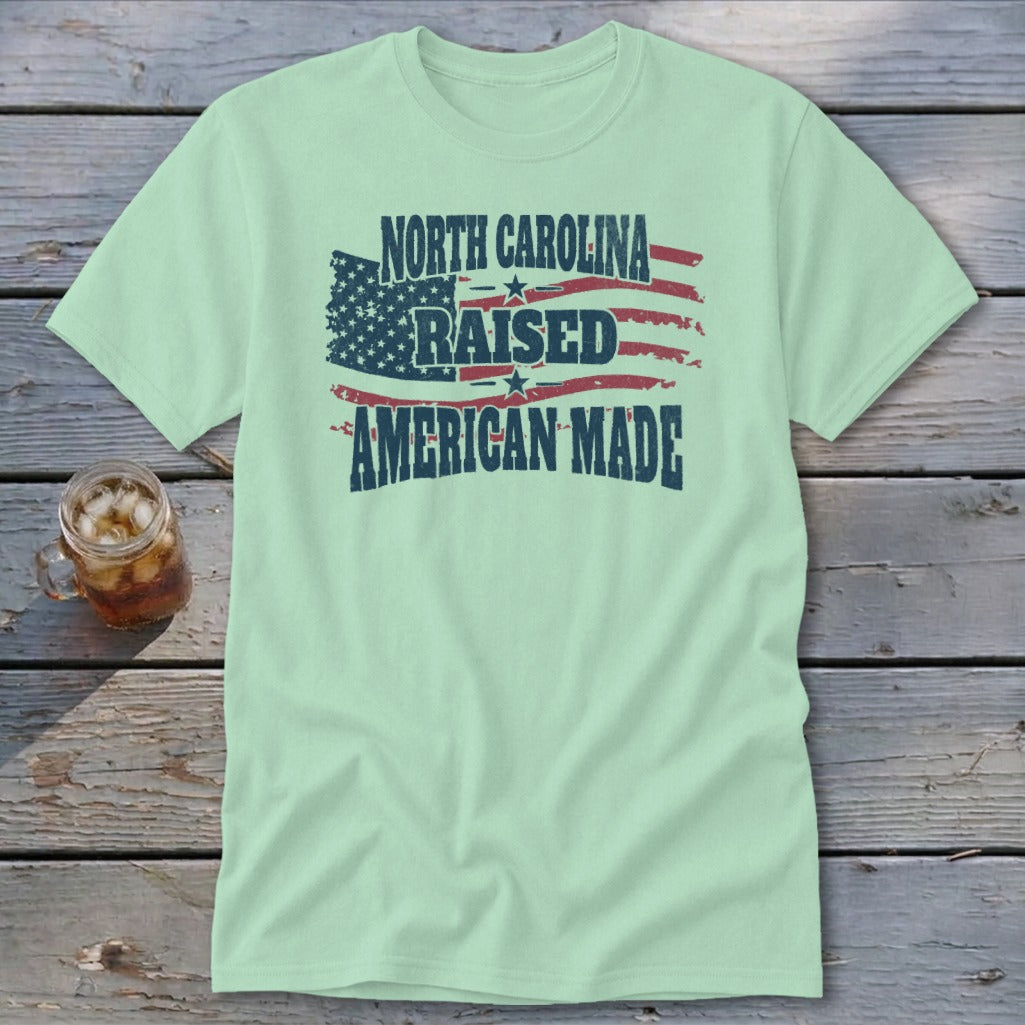 Light green t-shirt with distressed American flag graphic and text that reads North Carolina Raised American Made.